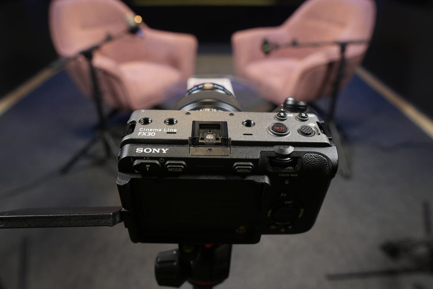 A Sony FX30 cinema camera on its tripod, facing the two pink armchairs