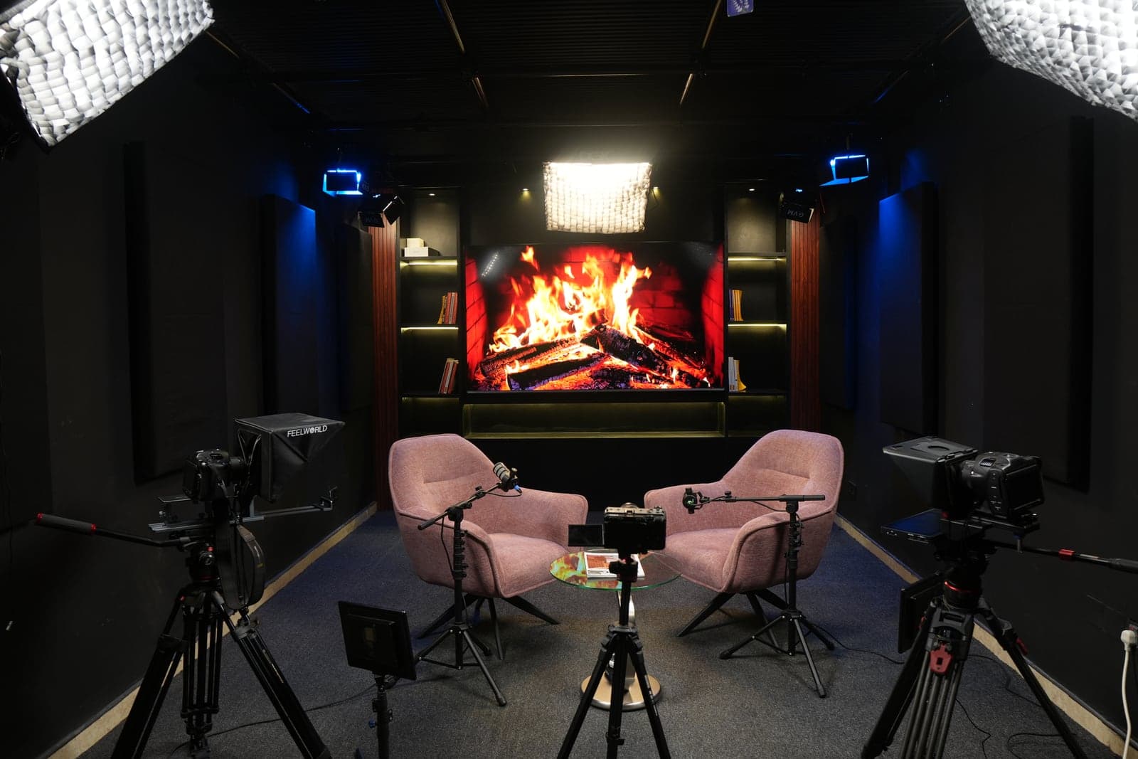 The full studio set: pink armchairs and a fireplace scene on the 100-inch screen, ringed by cameras, teleprompters and softbox lights