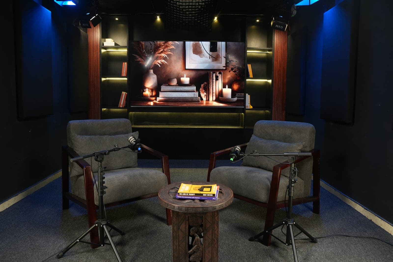 The second set: grey armchairs with microphones around a carved side table, with a candlelit scene on the screen