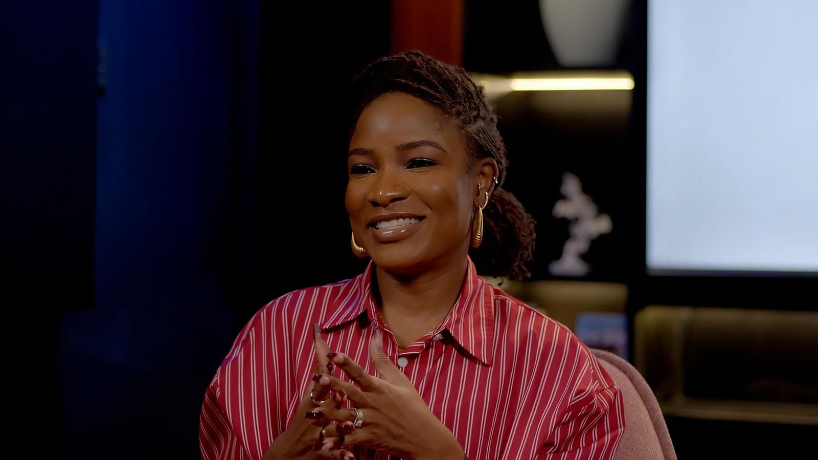 A smiling host in a red striped shirt, mid-conversation on the pink armchair set