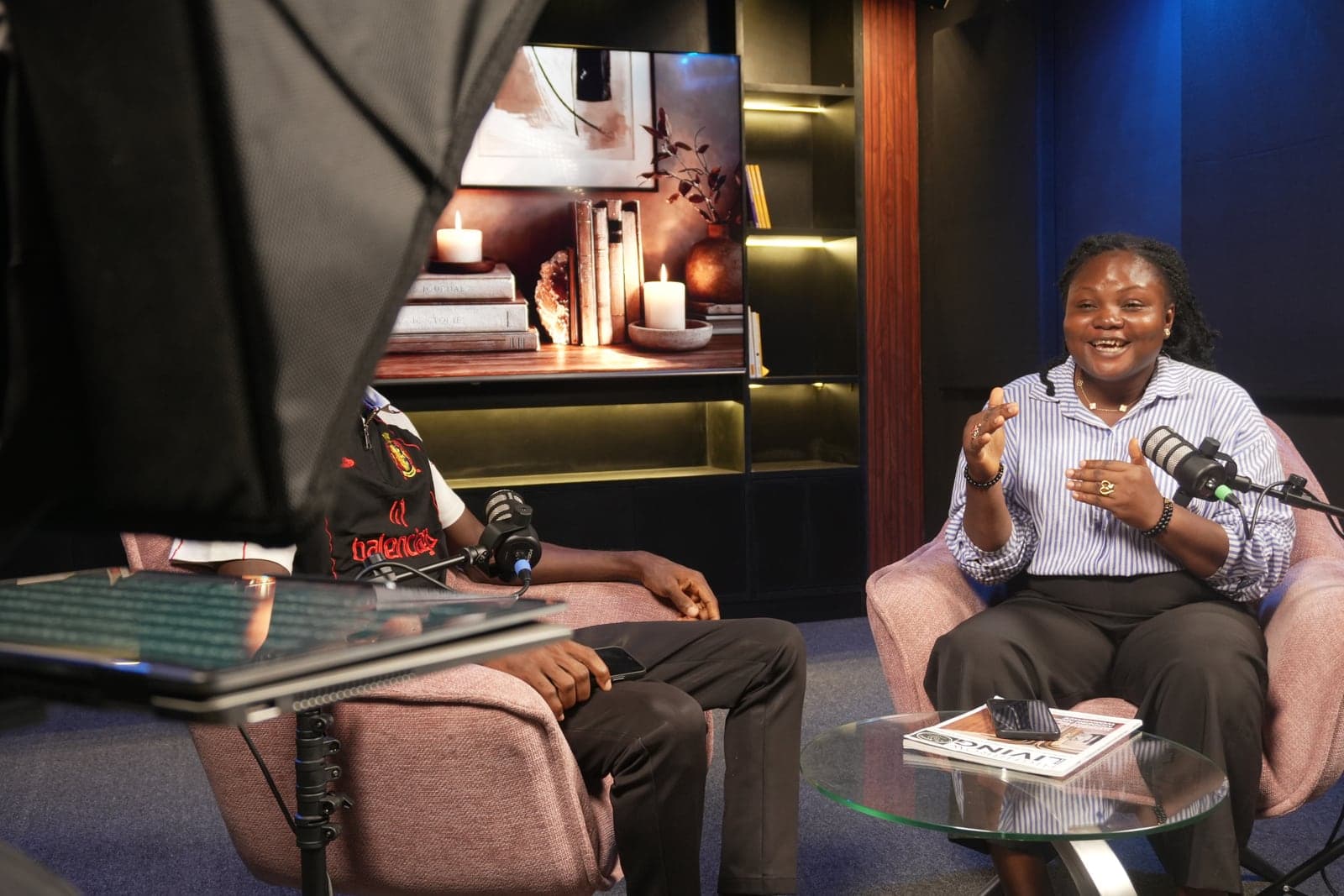 The teleprompter and a softbox light in the foreground, with a guest talking on set
